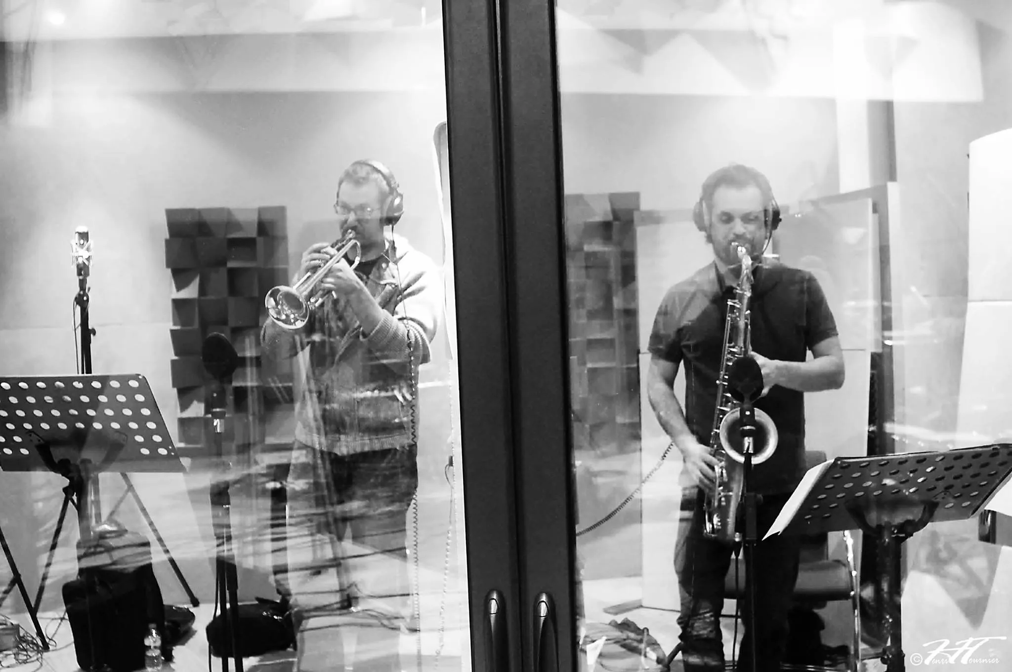 Trompettiste et saxophoniste en séance derrière la vitre de la cabine